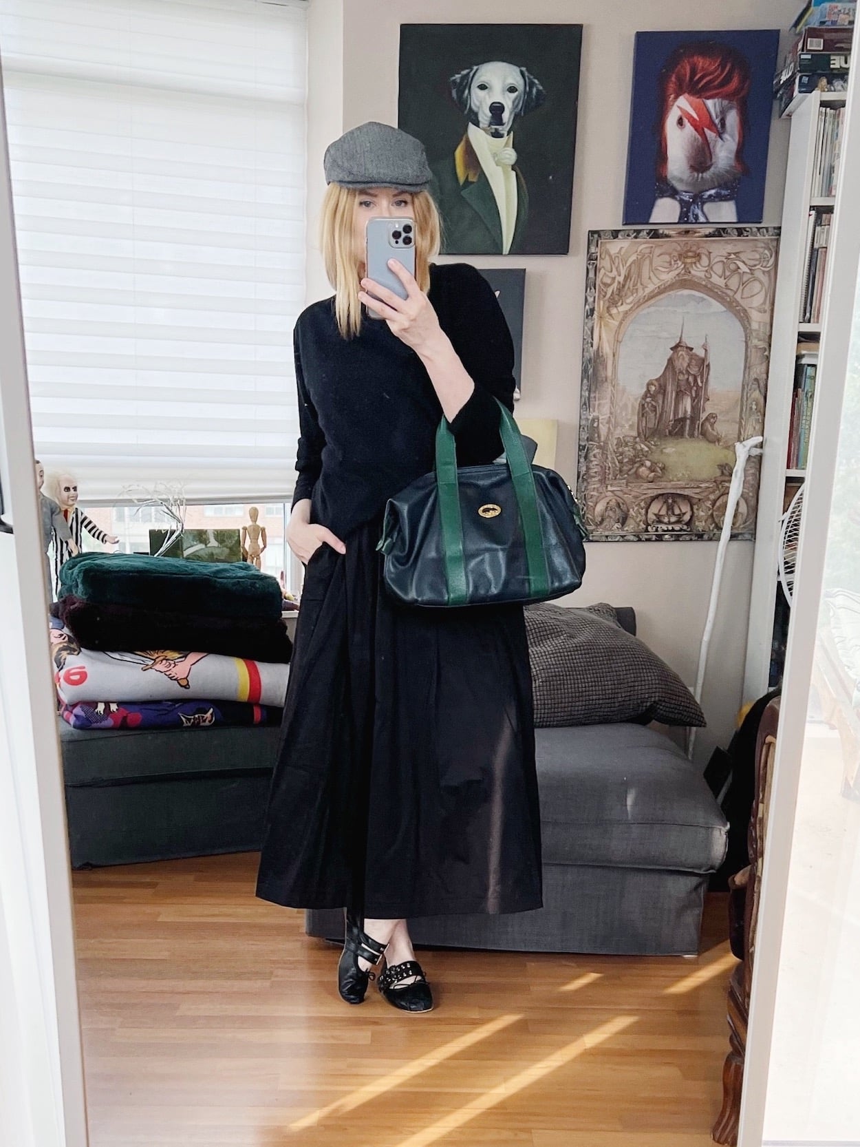 A blonde woman is wearing a black midi skirt with a black cashmere sweater, a grey flat cap, a vintage Longchamp handbag, and Miu Miu ballet flats.