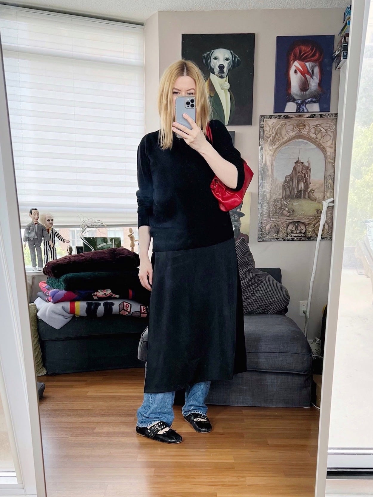 A blonde woman is wearing a slip dress over vintage Levis, with a black cashmere sweater layered over the top. Miu Miu ballet flats, and a red vintage Prada handbag.