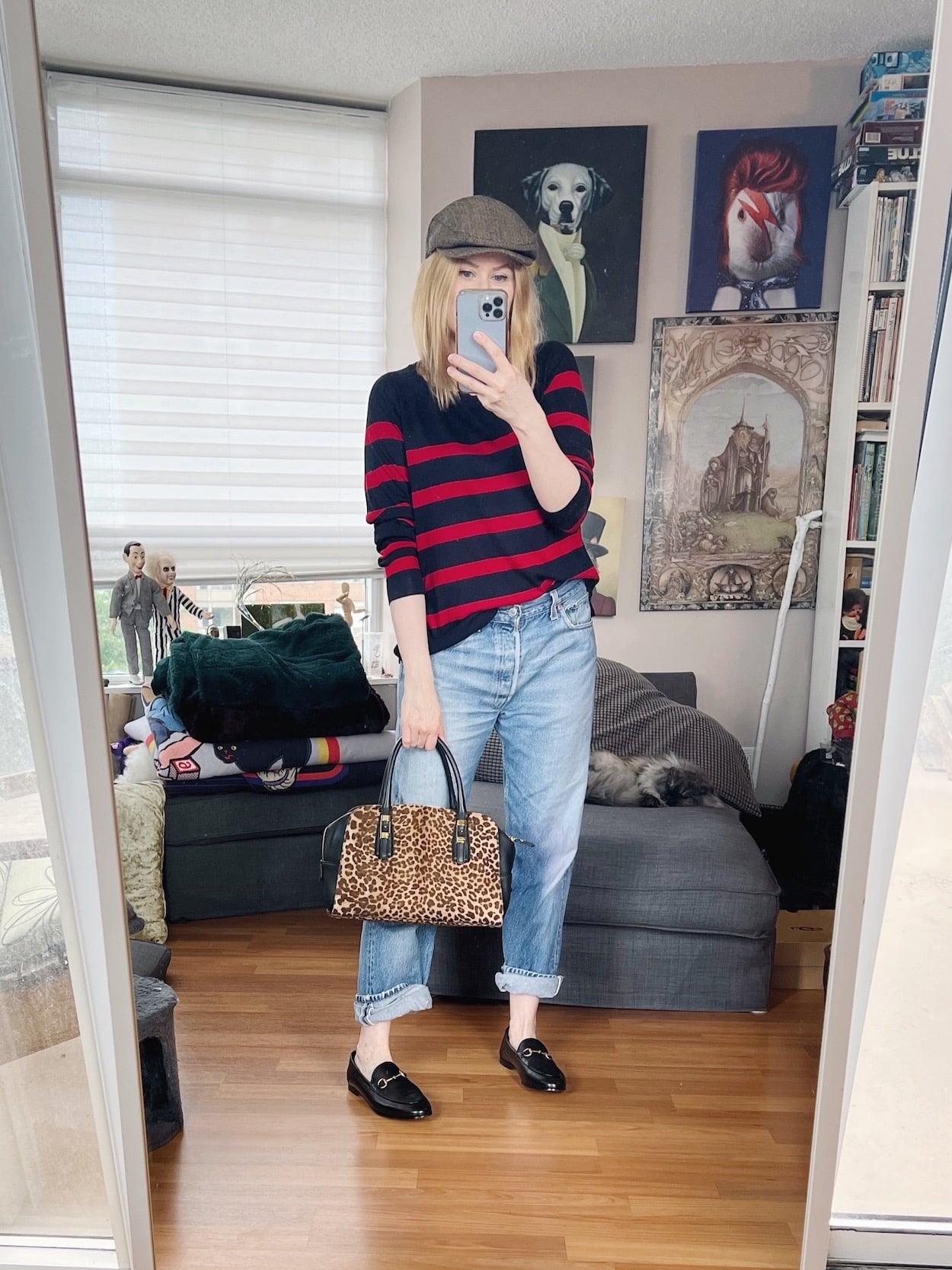 A blonde woman is wearing a striped sweater, vintage Levi's, a flat cap, Gucci loafers, and an animal print Ferragamo handbag.