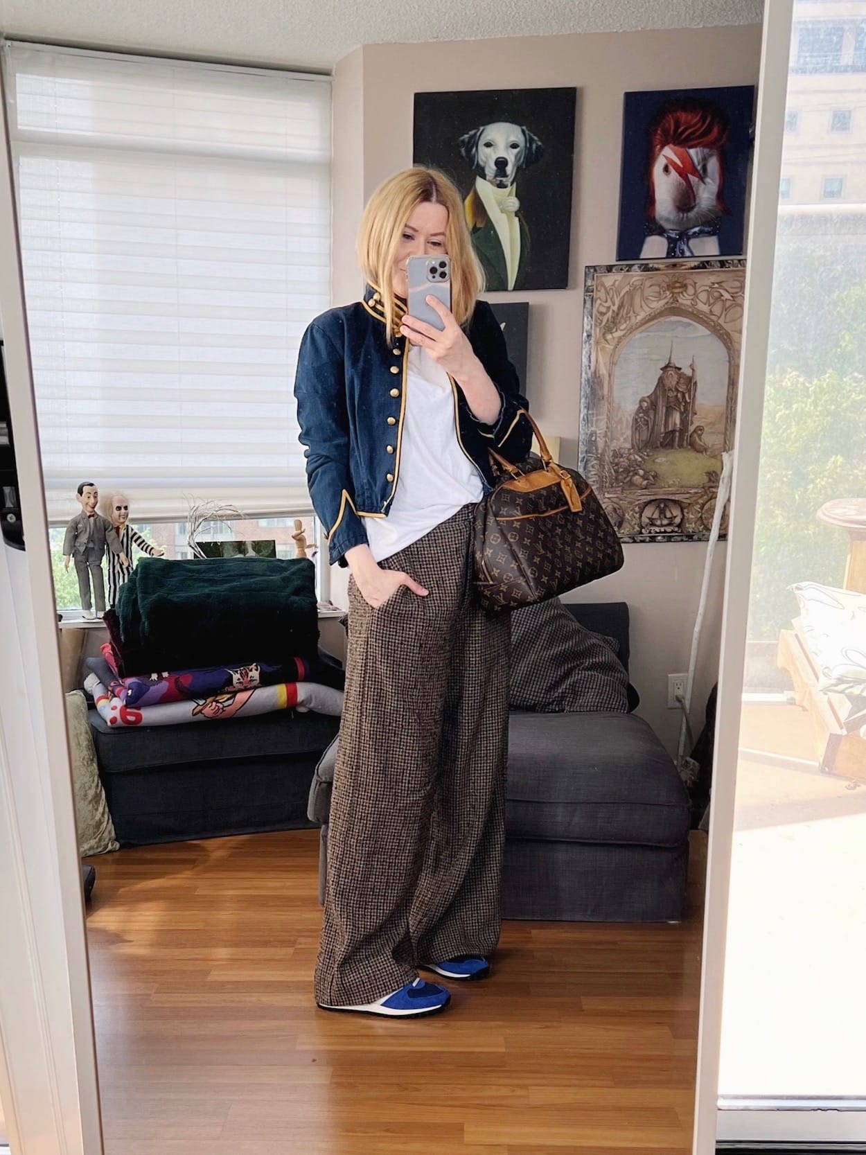 A blonde woman is wearing wide leg brown trousers, a white t-shirt, Ralph Lauren jacket, blue Adidas, and a vintage Louis Vuitton bag.