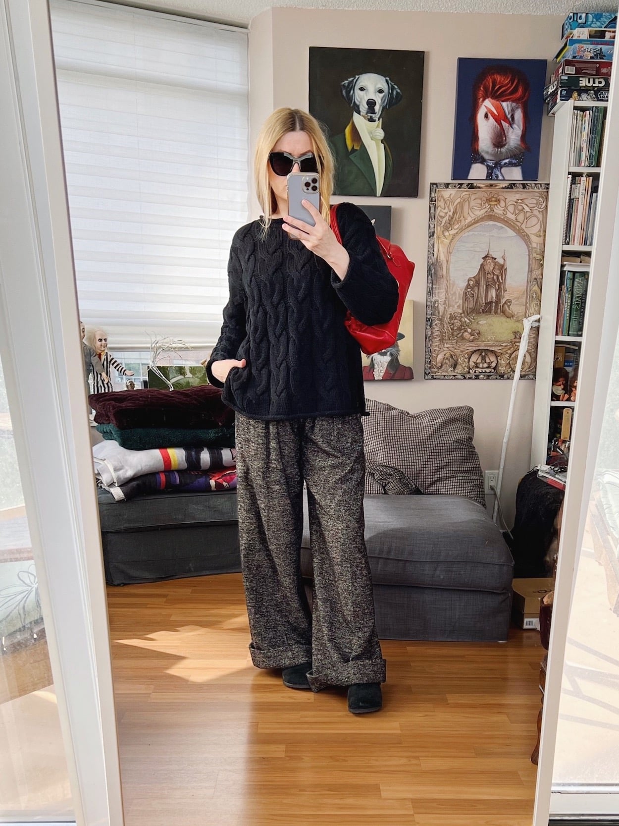 A blonde woman is wearing a black cable knit sweater, trousers, Birkenstock Bostons, black sunglasses, and a red Prada bag.