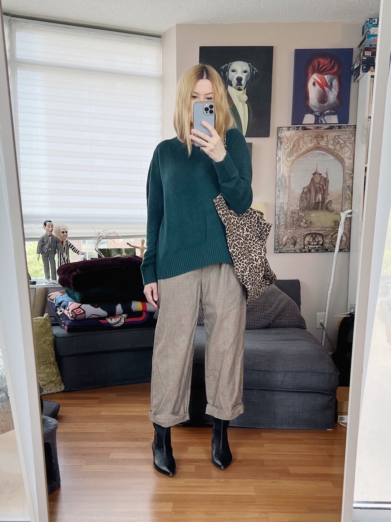 A blonde woman is wearing a green sweater, 90s Calvin Klein trousers, black boots, and an animal print tote.