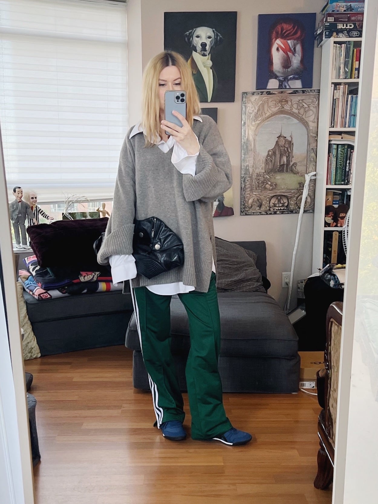 A blonde woman is wearing an oversized white button up layered under an oversized sweater, retro Adidas, Onitsuka Tiger sneakers, and an Alexander McQueen clutch.
