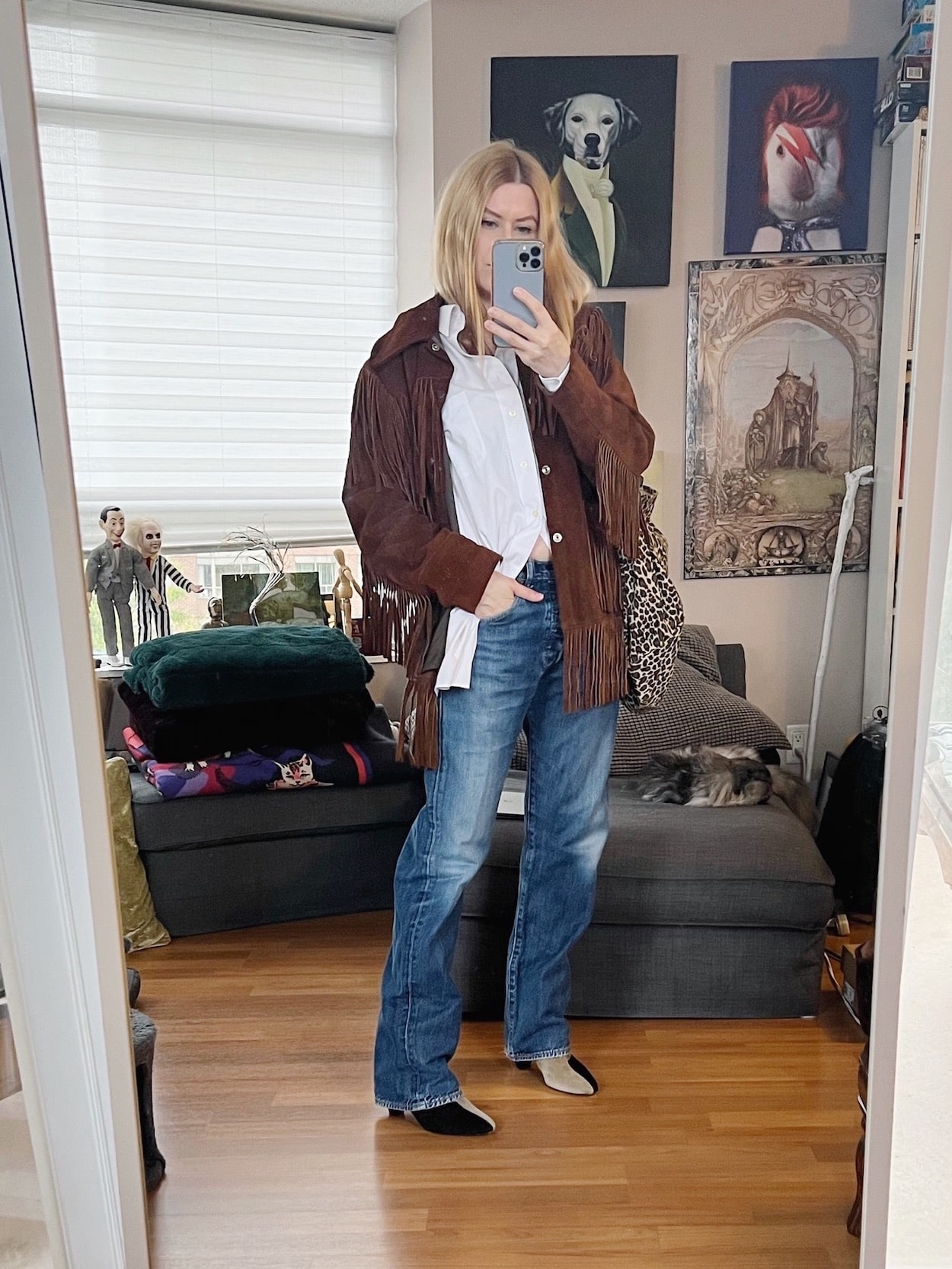 A blonde woman is wearing a white button up, vintage Levi's, Patch boots, a vintage fringe jacket, and is carrying an animal print tote.
