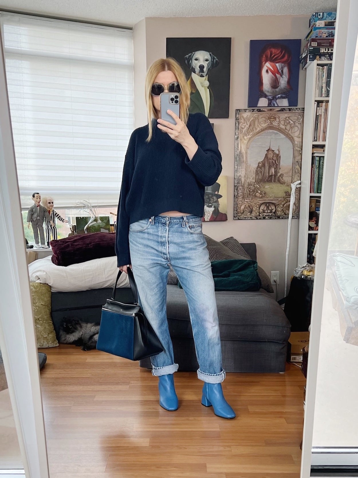 A blonde woman is wearing a navy blue sweater, vintage Levi's Blue boots, blue vintage sunglasses, and a Celine edge bag, also blue.