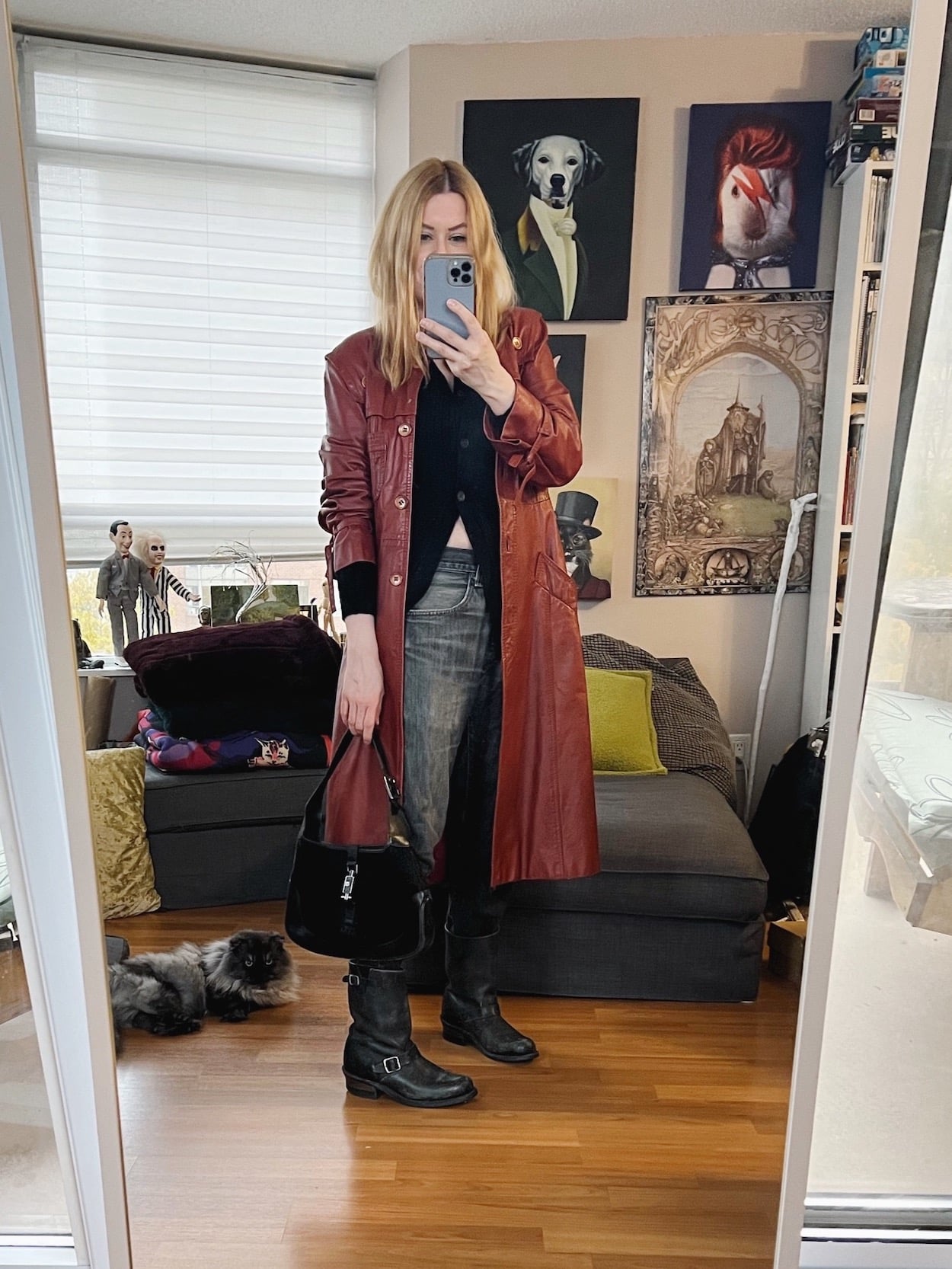 A blonde woman is wearing a black cardigan, vintage Levi's, A vintage leather trench, Frye Boots, and is carrying a vintage Gucci bag.