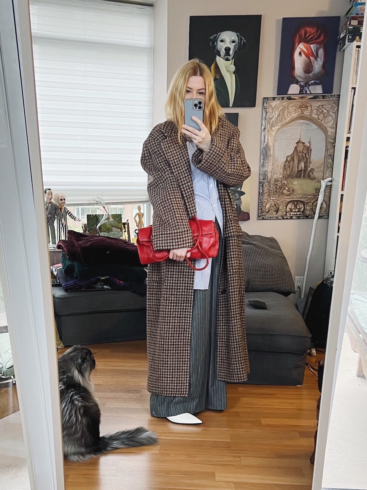 A blonde woman is wearing grey wide leg trousers, ao oversized button up, white booties, a 90s Ralph Lauren long coat, and has a vintage Prada handbag.