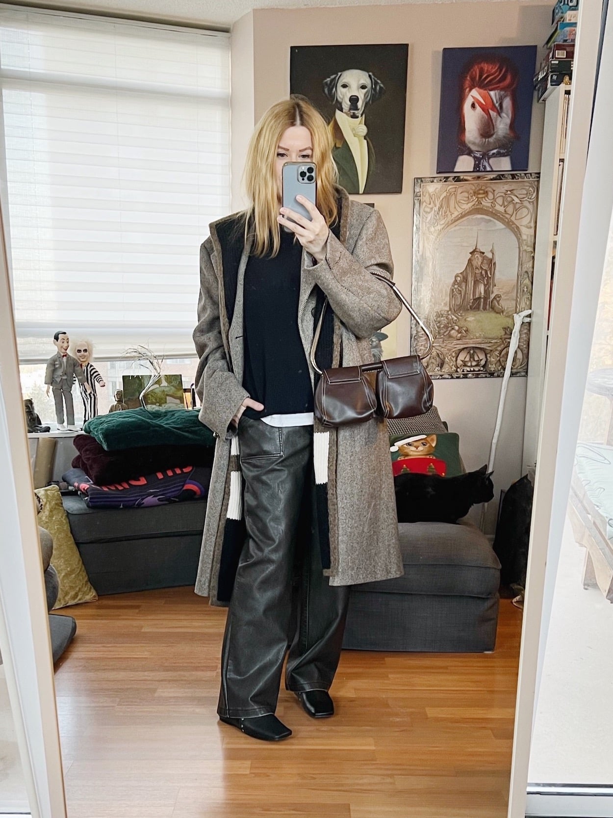 A blonde woman is wearing a cashmere sweater, faux leather trousers, a men's vintage 90s coat, old Celine boots, a hooded scarf, and a vintgae bag.