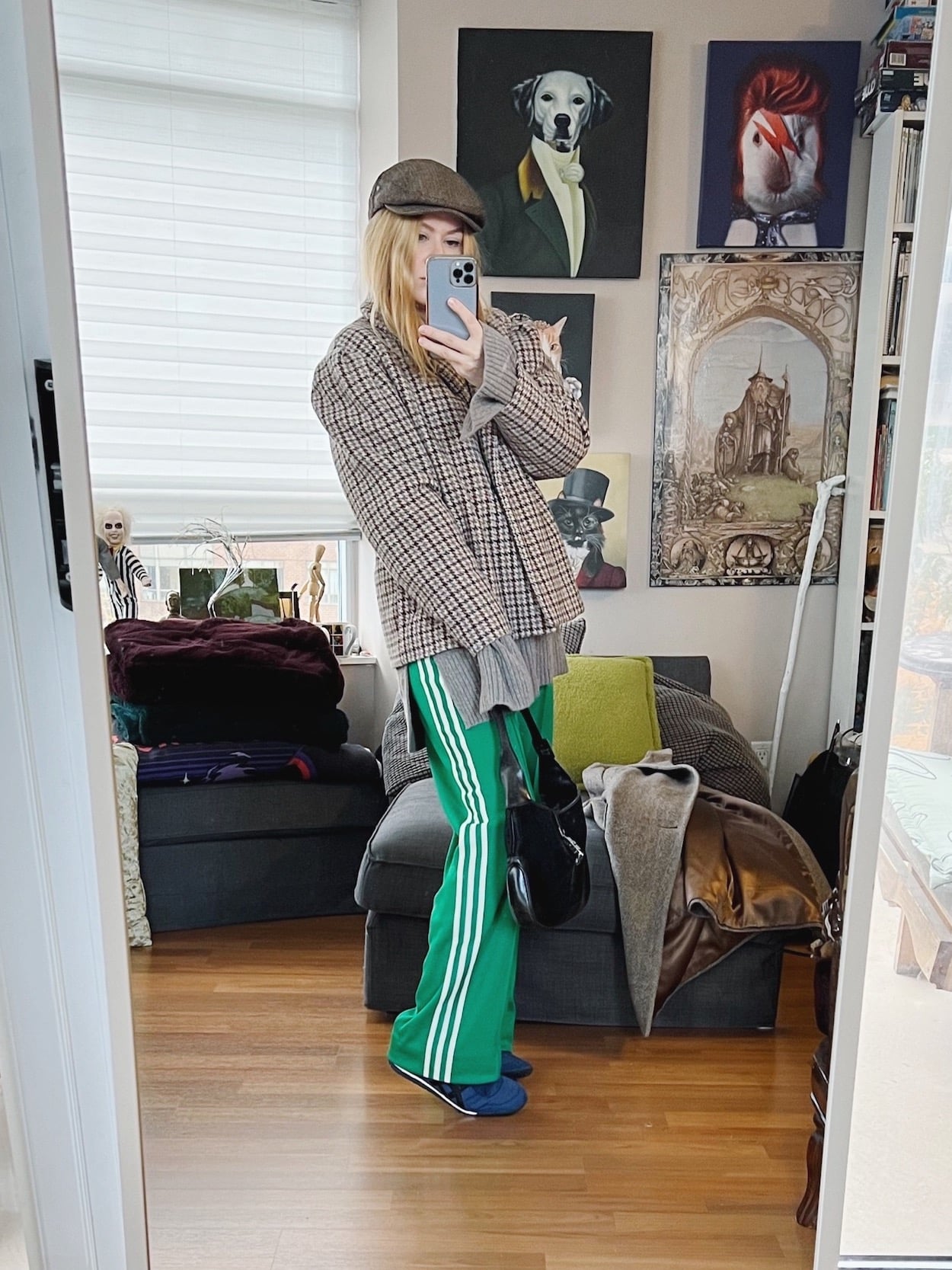 A blonde woman is wearing an oversized sweater, houndstooth jacket, Green adidas track pants, Onitsuka Tigers, a flat cap, and a vintage Gucci handbag.