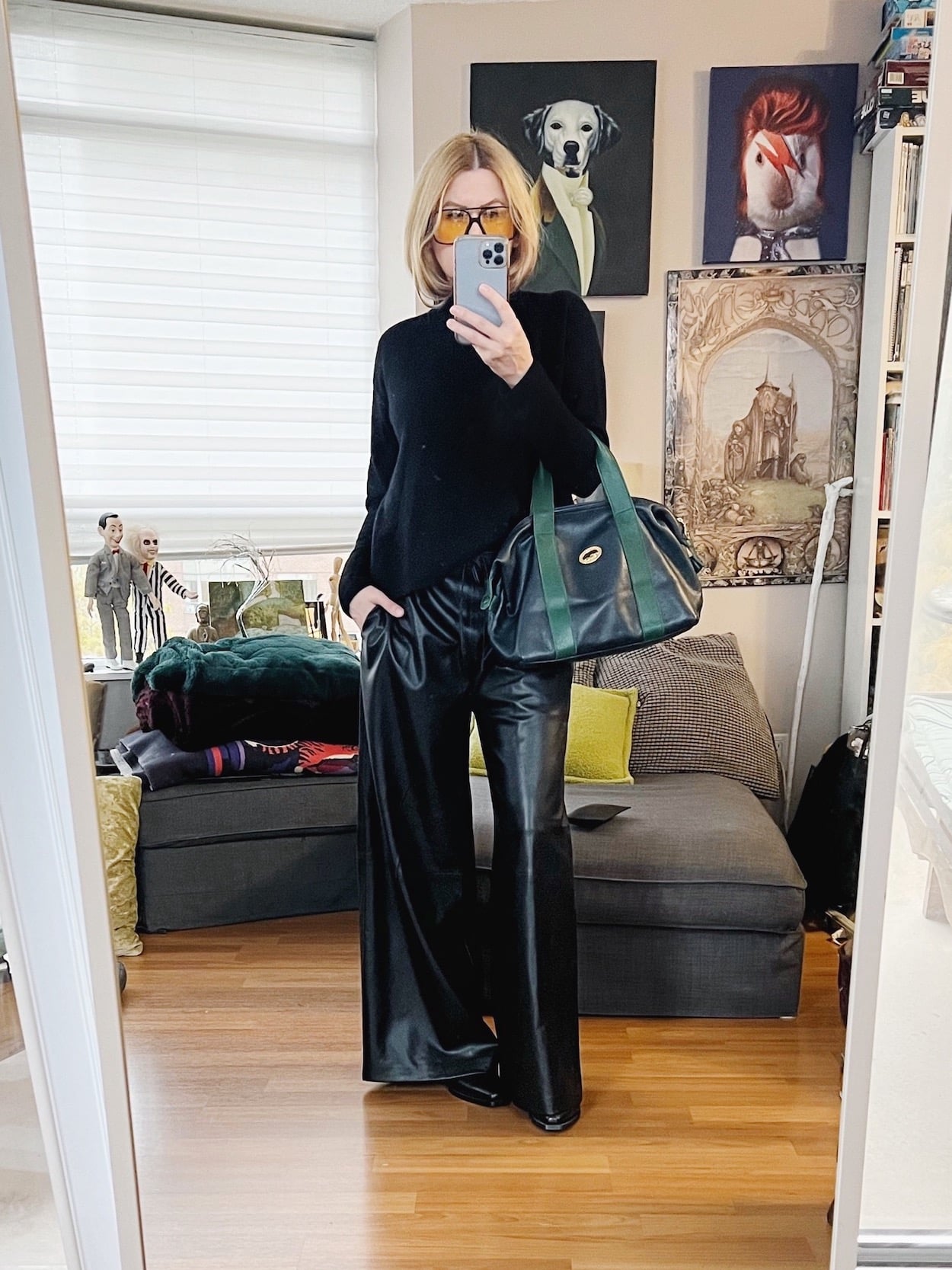A blonde woman is wearing a cashmere turtleneck sweater, leather pants, western boots, retro sunglasses, and is carrying a vintage Longchamp bag.
