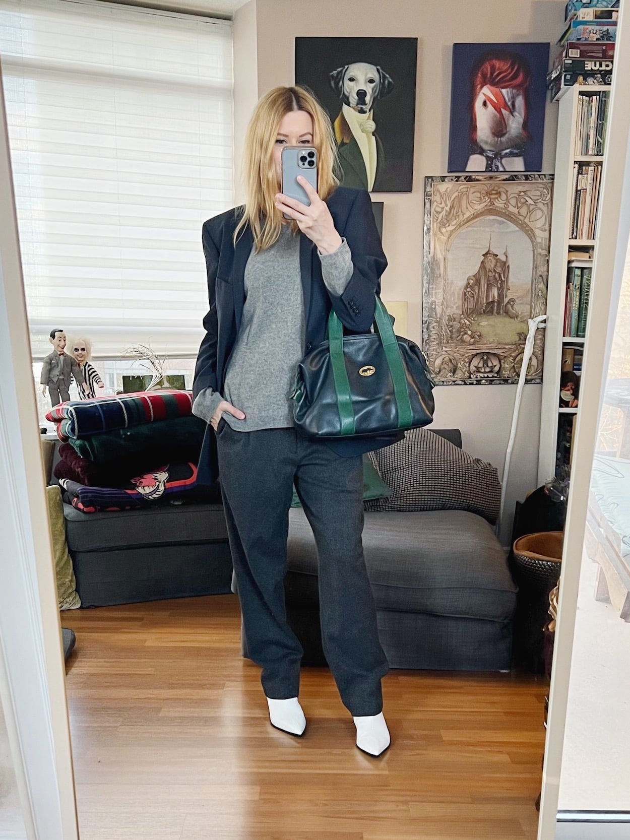 A blonde woman is wearing a grey cashmere sweater, gret trousers, a navy blue blazer, white booties, and a vintage Longchamp bag.