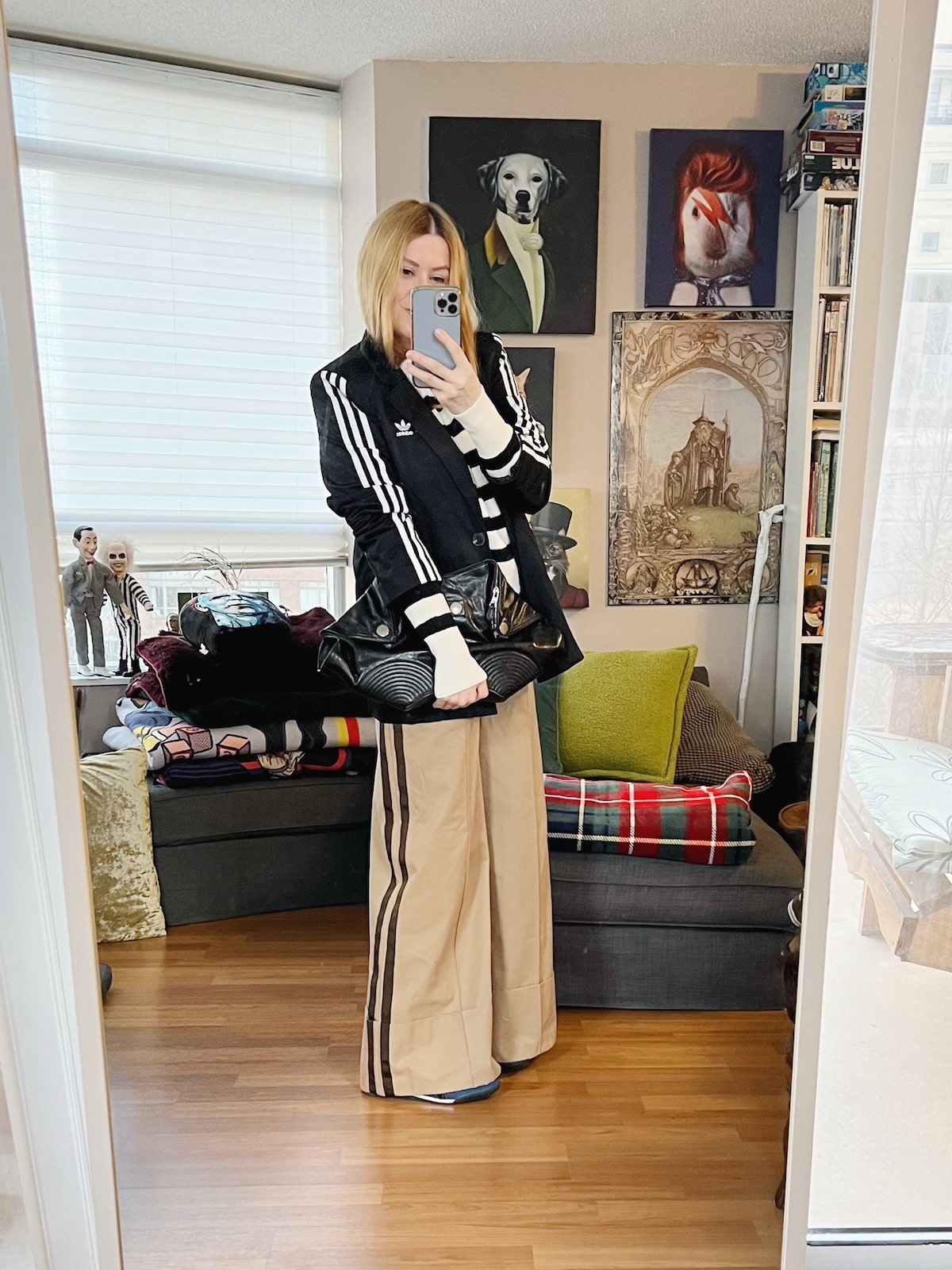 A blonde woman is wearing a strioed sweater, Adidas blazer, wide leg trousers, sneakers, and is carrying an Alexander McQueen clutch.