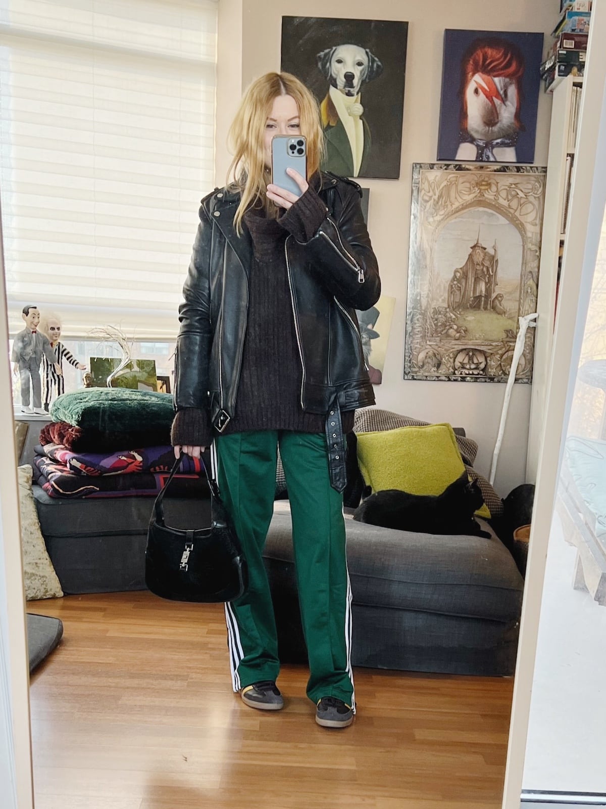 A blonde woman is wearing a sweater, adidas track pants, an oversized moto jacket, sneakers, and a vintage Gucci bag.