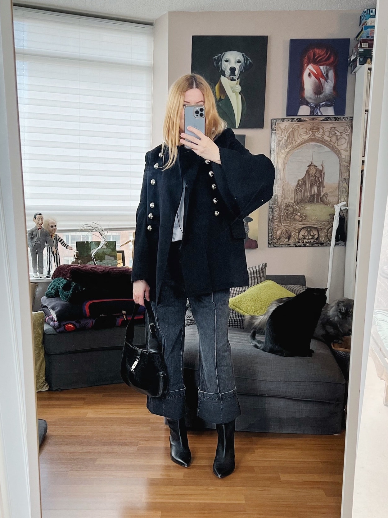 A blonde woman is wearing a bell sleeve coat, cuffed jeans, a white t-shirt, black boots, and a vintage Gucci bag.