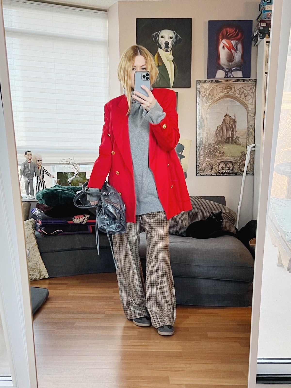 A blonde woman is wearing a grey turtleneck sweater under a bright red blazer, houndstooth pants, sneakers, and a Balenciaga bag.