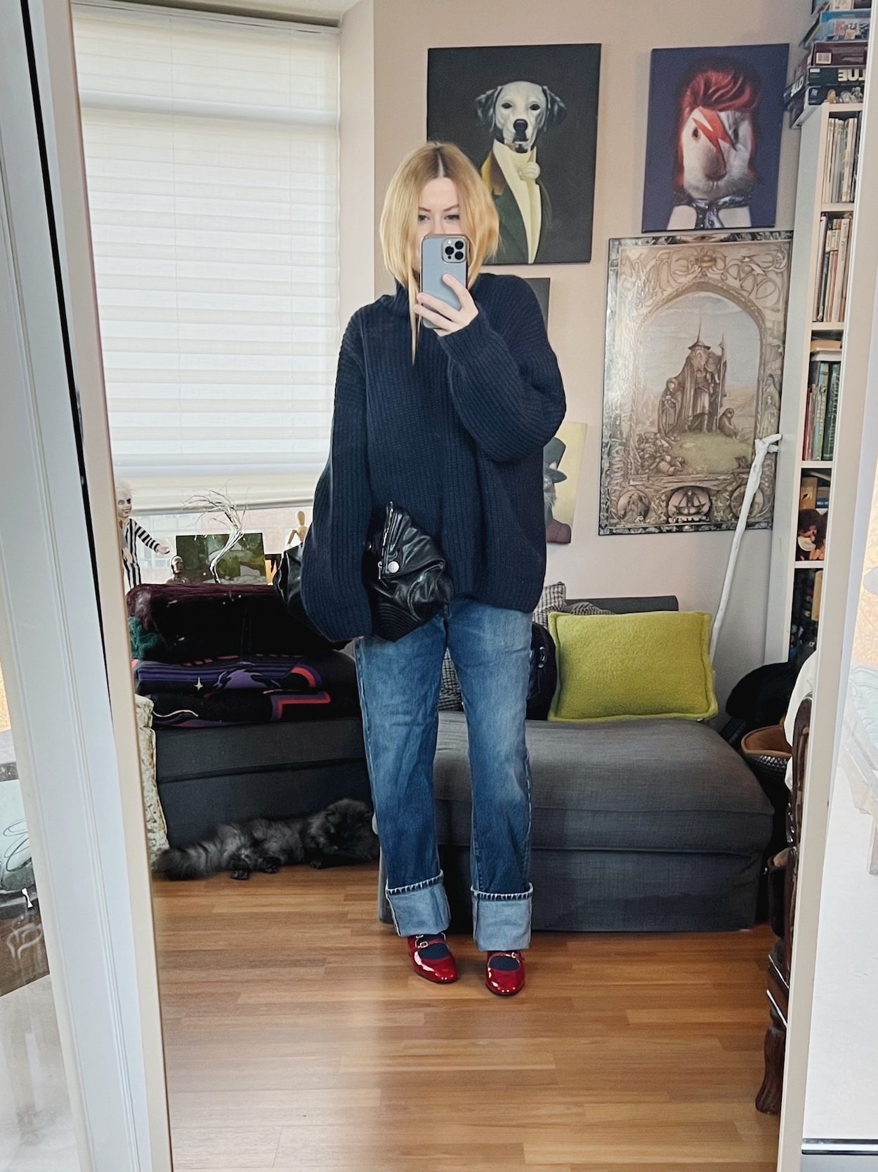 A blonde woman is wearing an Anine Bing sweater, vintage Levi's, red Mary Janes, and an Alexander McQueen clutch.