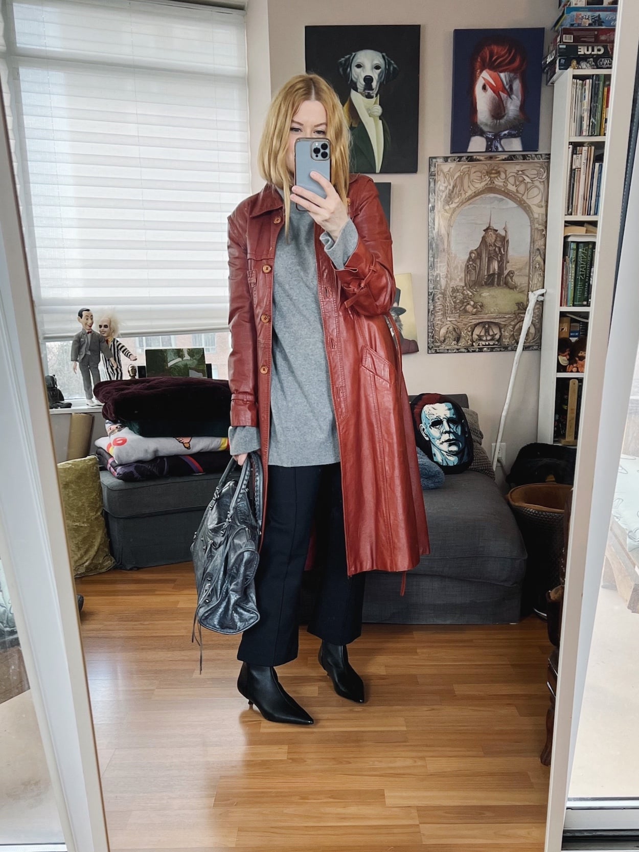 Sara of livelovesara is standing in front of a mirror taking a photo of her outfit. She is wearing a long grey turtleneck sweater, kick flares, a vintage trench, black boots, and a grey Balenciaga bag.