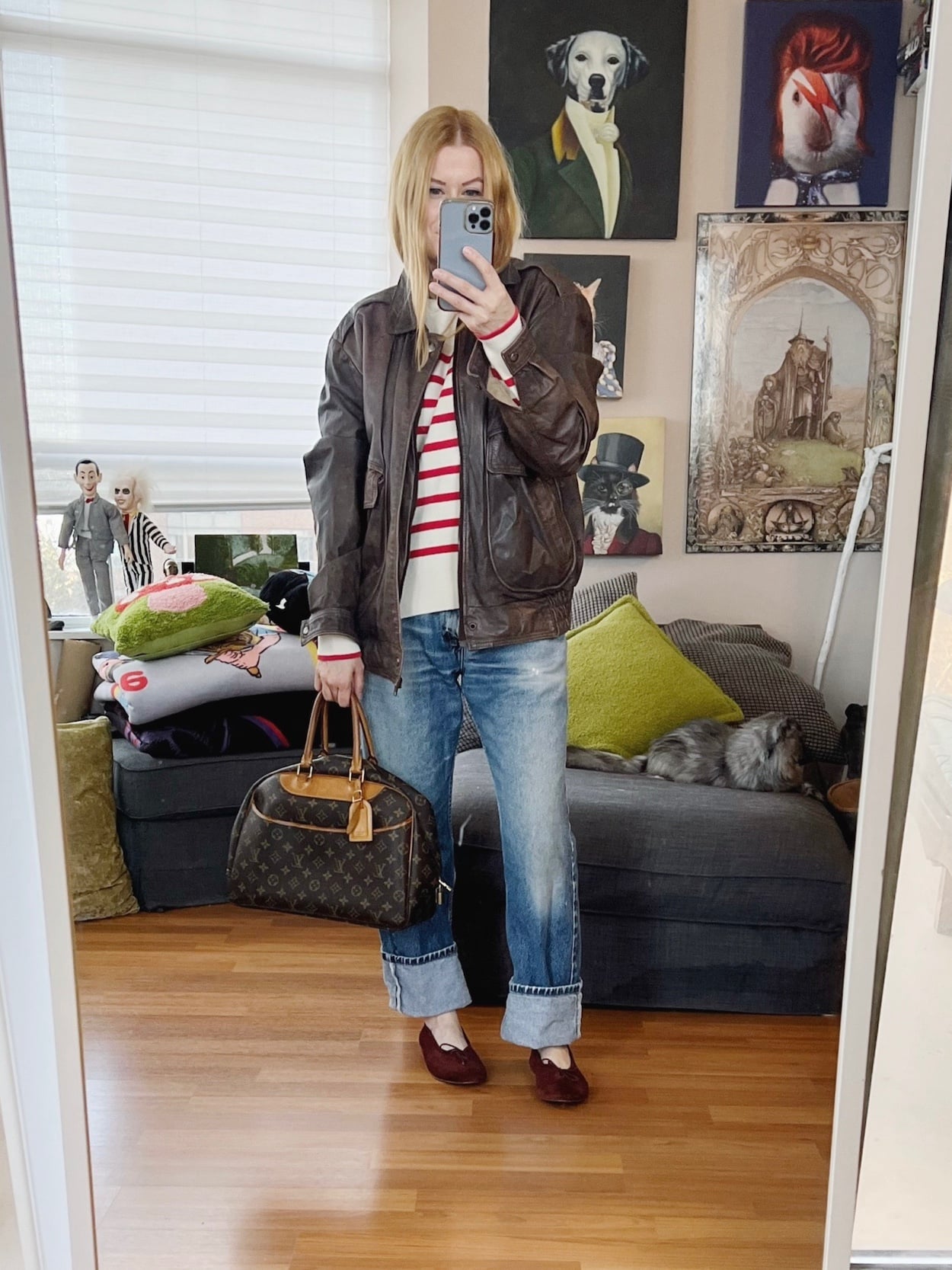 Sara of livelovesara is standing in front of a mirror taking a photo of her outfit. She is wearing a cream and red striped sweater with vintage levis. Over the top she is wearing a vintage men's aviator jacket, paired with brown ballet flats, and is holding a vintage Louis Vuitton bag.