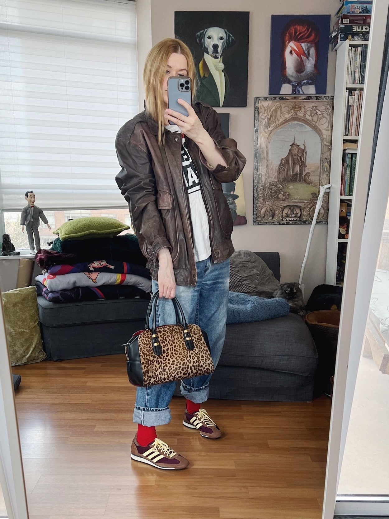 Sara of livelovesara is standing in front of a mirror taking a photo of her outfit. She is wearing a Vision Streetwear t-shirt, vintage Levis, a vintage aviator jacket, Adidas sneakers, and an animal print bag.