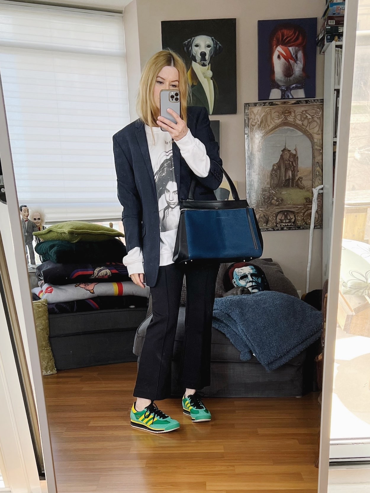 Sara of livelovesara is standing in front of a mirror taking a photo of her outfit. She is wearing black kick flares, a PJ Harvey Sweatshirt, men's navy blue blazer, Green sneakers, and is carrying a blue old Celine bag.