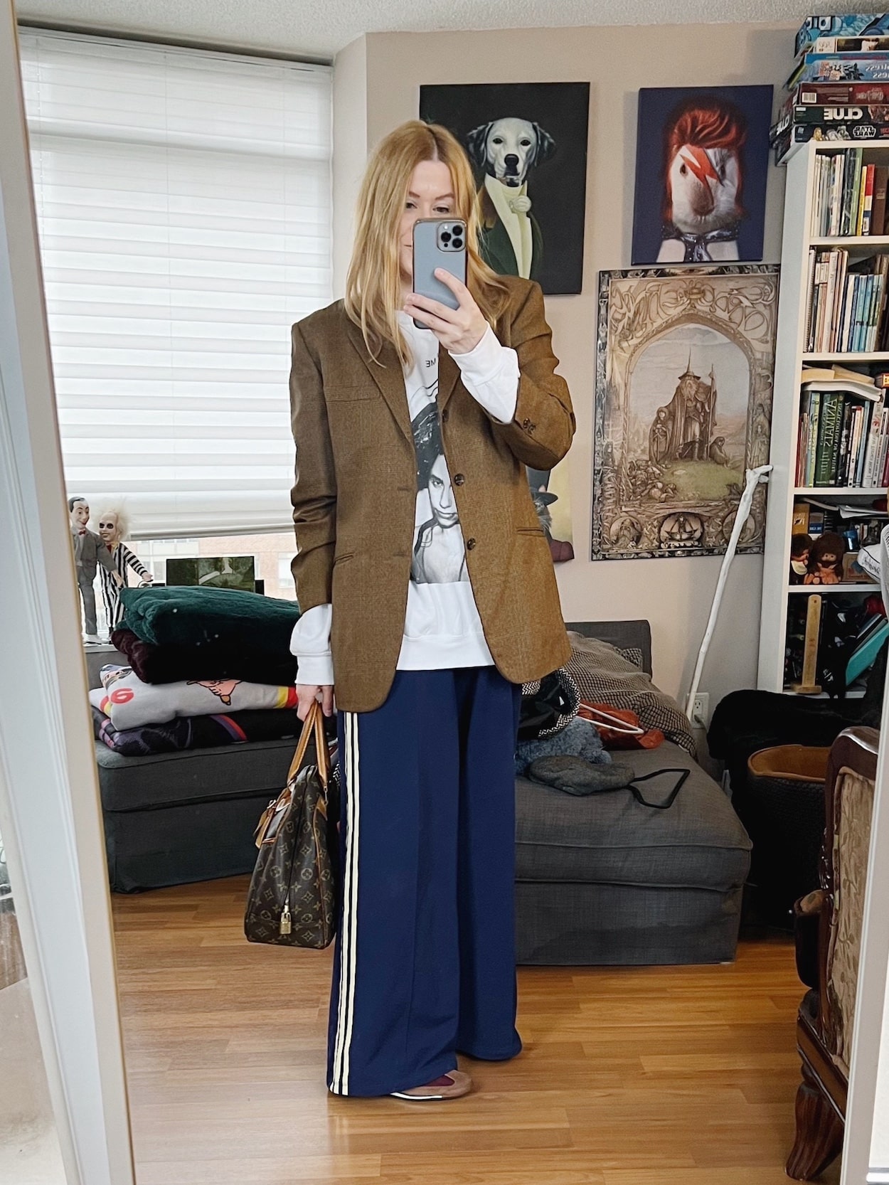 Sara of livelovesara is standing in front of a mirror taking a photo of her outfit. She is wearing a PJ Harvey sweatshirt under a vintage blazer, paired with blue wide leg Adidas track pants, brown Adidas SL 72 sneakers, and a vintage Louis Vuitton bag.