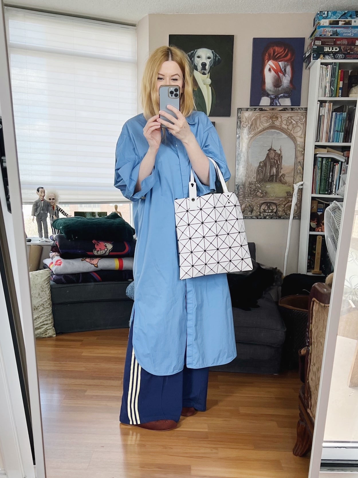 Sara of livelovesara is standing in front of a mirror taking a photo of her outfit. She is wearing a long, blue button up shirt dress over blue adidas track pants, brown ballet flats, and is carrying a white Issey Miyake bag.