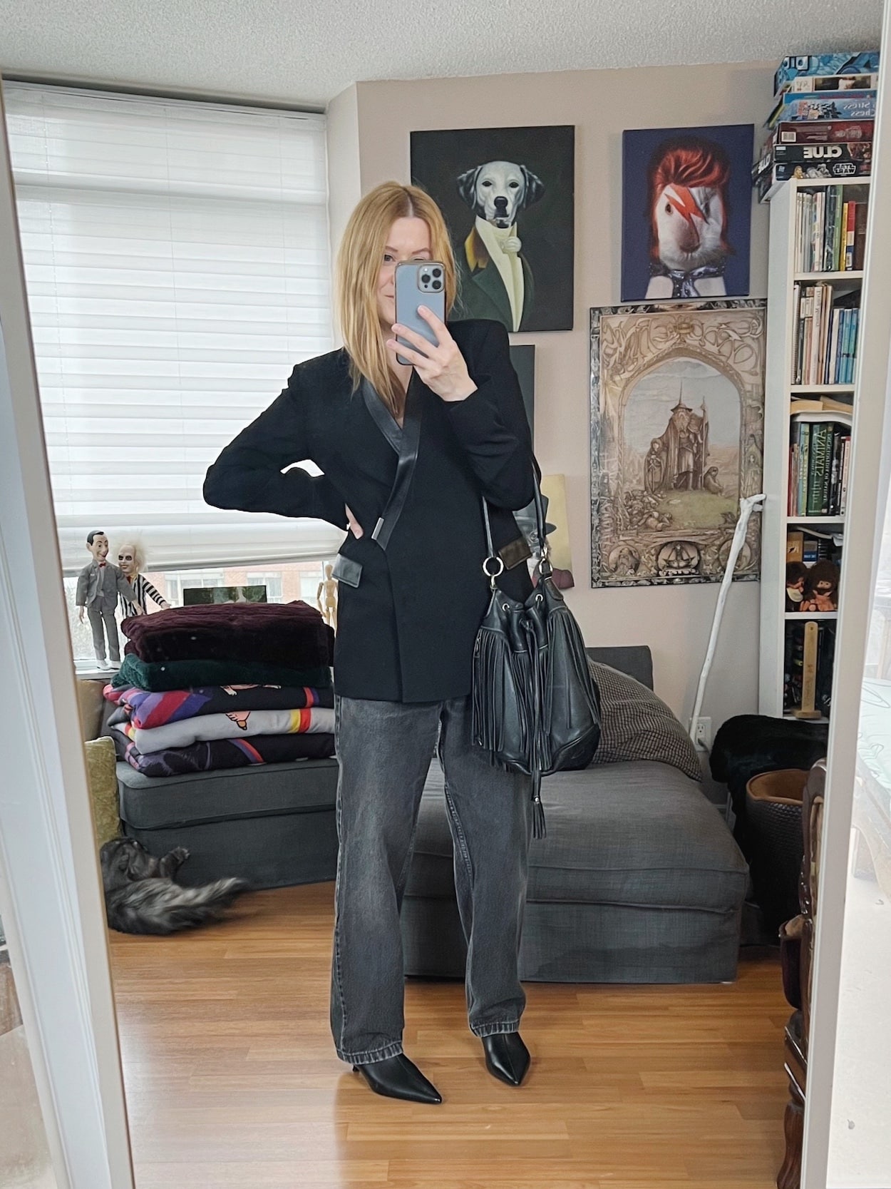 Sara of livelovesara is standing in front of a mirror taking a photo of her outfit. She is wearing a vintage black blazer with black vintage Levi's, black boots, and a vintage fringed bucker bag.