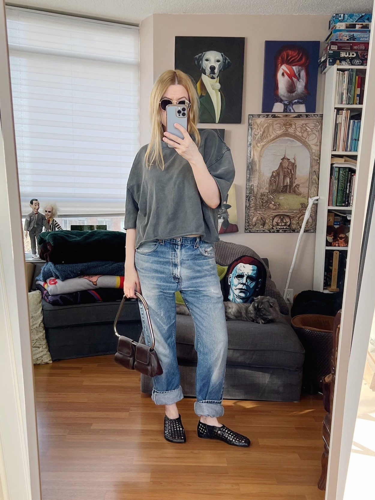 Sara of livelovesara is standing in front of a mirror taking a photo of her outfit. She is wearing a grey short sleeve sweatshirt, vintage jeans, woven flats, 90s sunglasses, and a vintage handbag.