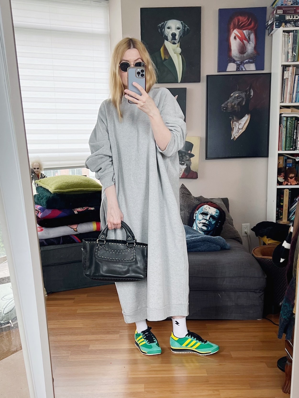 Sara of livelovesara is standing in front of a mirror taking a photo of her outfit. She is wearing a, oversized sweatshirt dress, Adidas SL72s, reton sunglasses, and a vintage Celine Boogie bag.