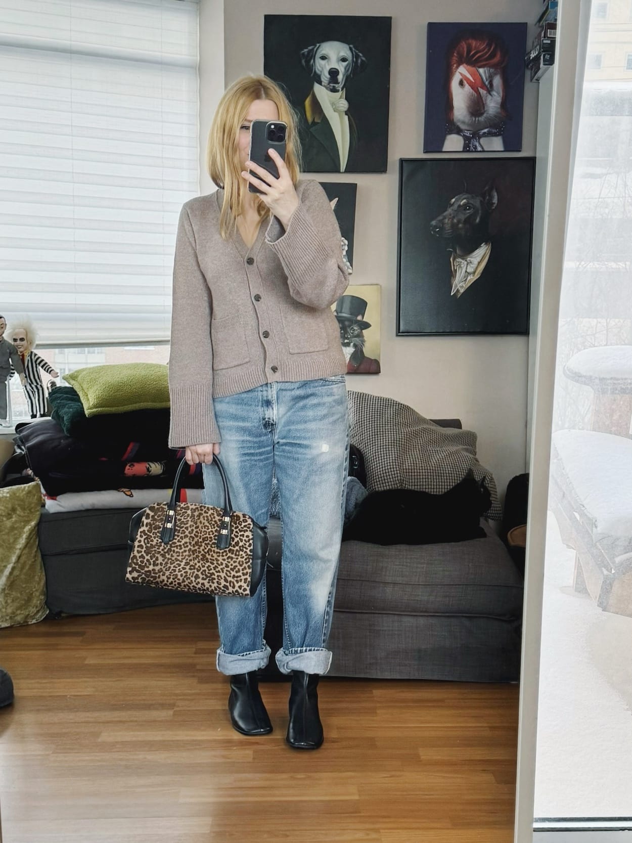 Sara of livelovesara is standing in front of a mirror taking a photo of her outfit. She is wearing a light brown cardigan, vintage Levis, flat black boots, and an animal print bag.