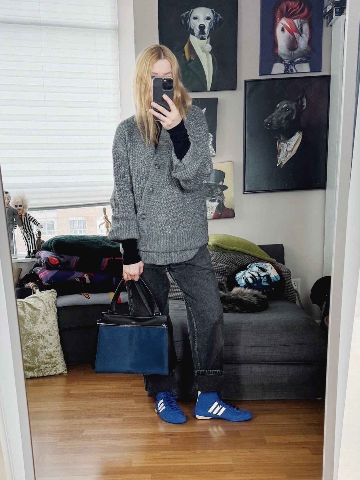 Sara of livelovesara is standing in front of a mirror taking a photo of her outfit. She is wearing a black turtleneck under an asymmetrical cardigan, black vintage jeans, blue Adidas Rasant, and an Old Celine Edge bag.