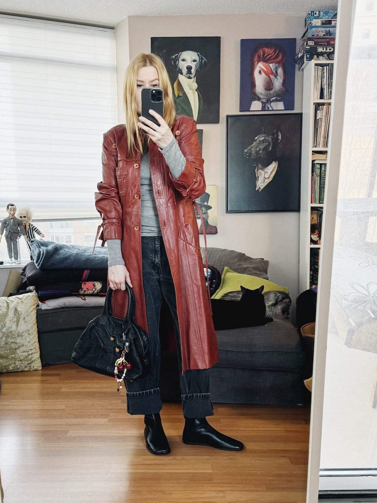 Sara of livelovesara is standing in front of a mirror taking a photo of her outfit. She is wearing a grey turtleneck under an orange vintage leather trench, black vintage Levis, black flats boots, and a YSL Easy bag.