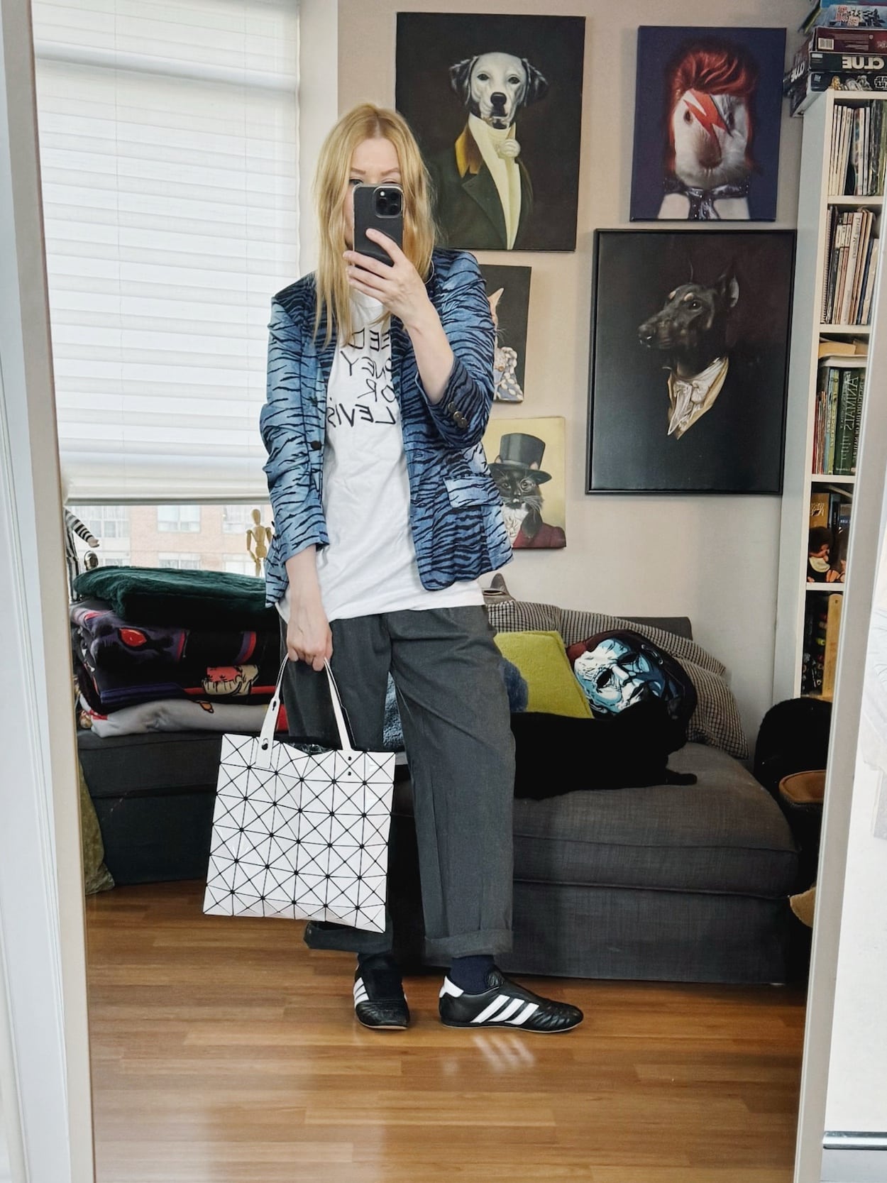 Sara of livelovesara is standing in front of a mirror taking a photo of her outfit. She is wearing a vintage tee under a tiger print blazer, trousers, Adidas Taekwondo sneakers, and an Issey Miyake bag.