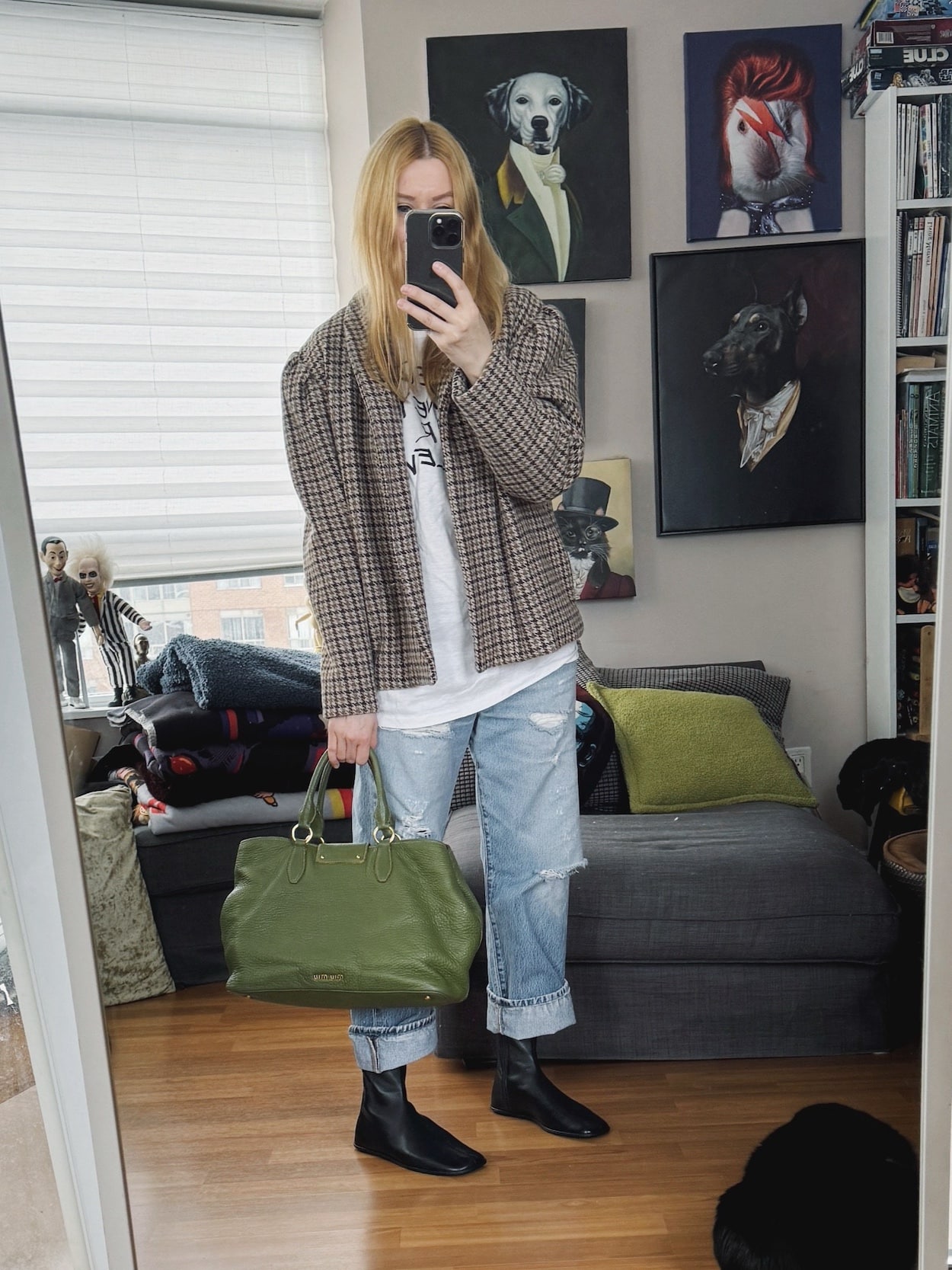 Sara of livelovesara is standing in front of a mirror taking a photo of her outfit. She is wearing an vintage tee under a isabel Marant jacket, vintage Levis, black boots, and a green tote.