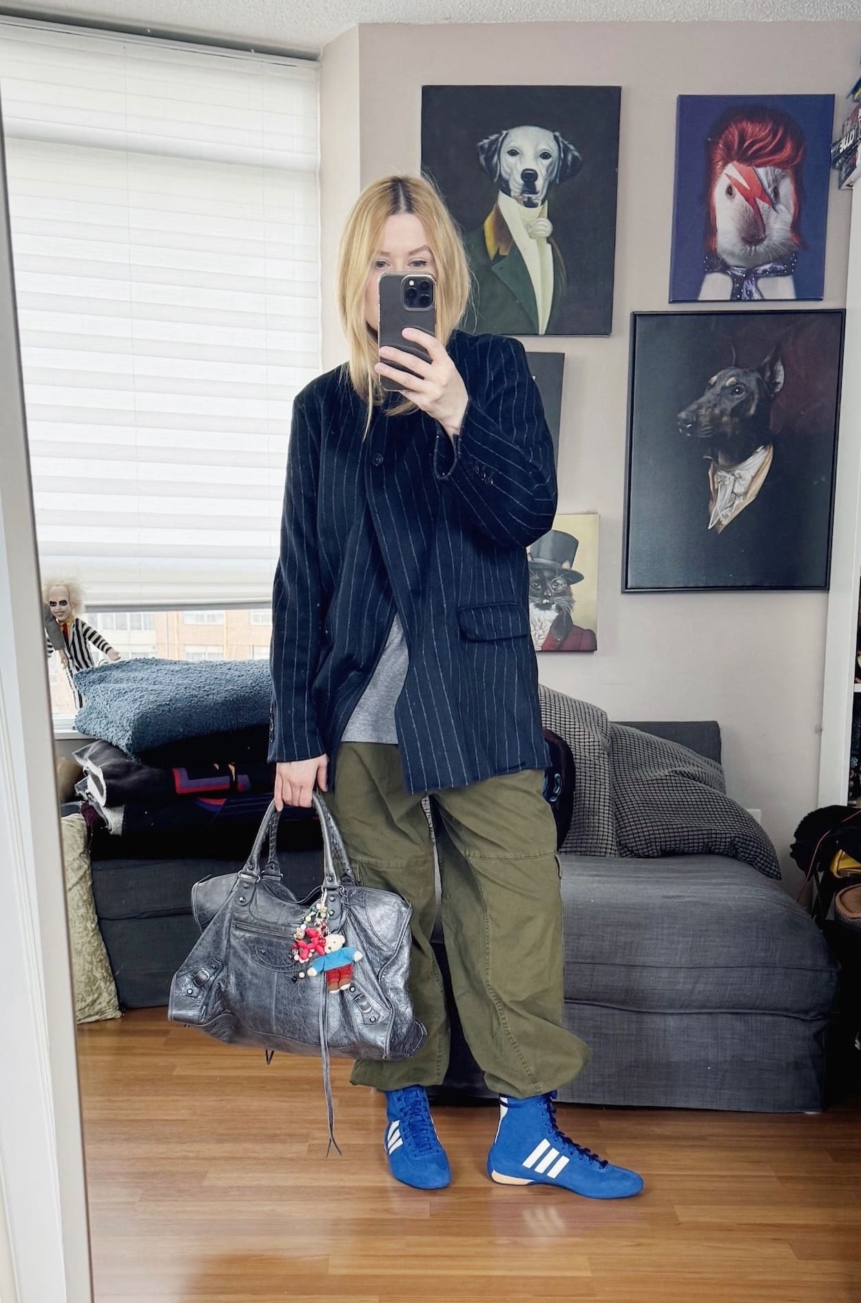 Sara of livelovesara is standing in front of a mirror taking a photo of her outfit. She is wearing a grey tee under a navy pinstripe blazer, green cargos, blue Adidas Rasant sneakers, and a Balenciaga grey bag.