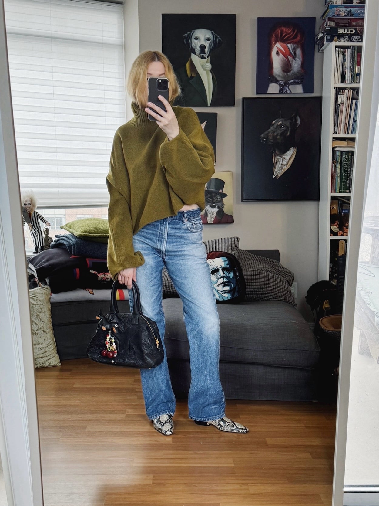 Sara of livelovesara is standing in front of a mirror taking a photo of her outfit. She is wearing a green sweater with vintage Lev's 517s, snake print boots, and a YSL easy bag.