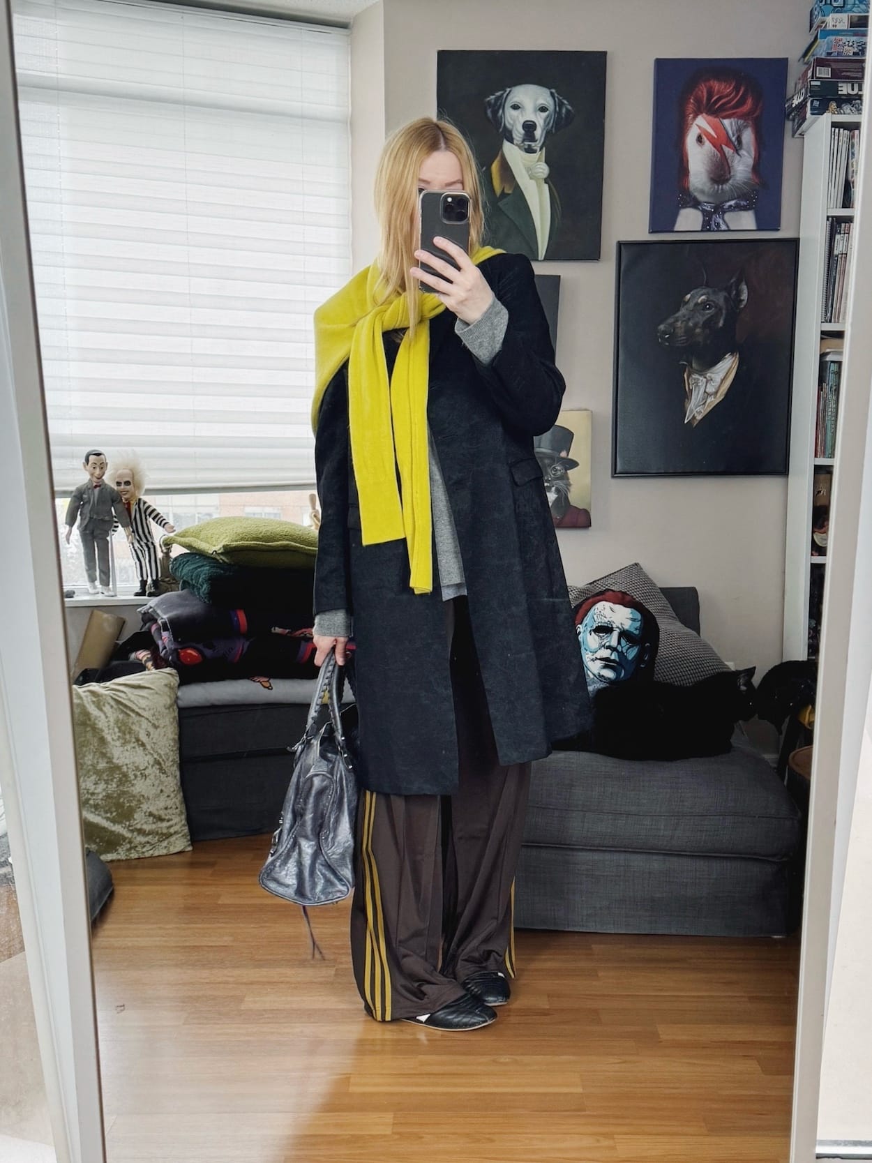 Sara of livelovesara is standing in front of a mirror taking a photo of her outfit. She is wearing a grey sweater with brown Adidas track pants, a vintage Dries Van Noten coat with a yellow sweater over the shoulder, Adidas Taekwondo sneakers, and a grey Balenciaga bag.
