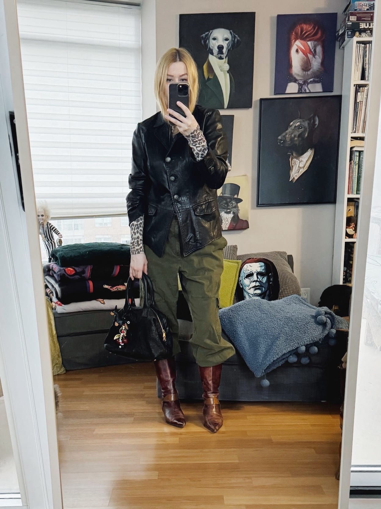Sara of livelovesara is standing in front of a mirror taking a photo of her outfit. She is wearing an animal print turtleneck under a vintage leather jacket, cargos tucked into vintage jeans, and a YSL Easy bag.