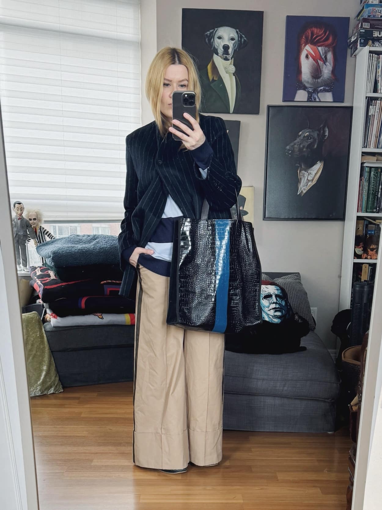Sara of livelovesara is standing in front of a mirror taking a photo of her outfit. She is wearing a light blue and navy striped sweater under a navy pinstrip jacket, tan trousers, Adidas Taekwondo, and a Dris Van Noten striped tote.