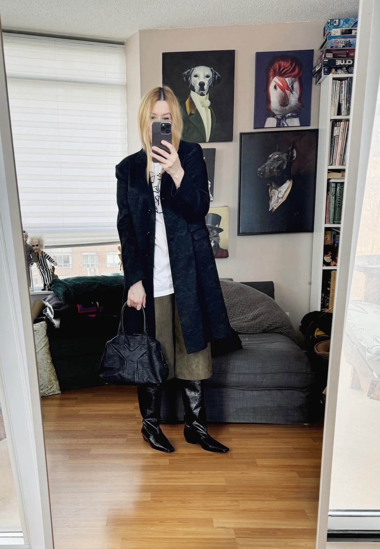 Sara of livelovesara is standing in front of a mirror taking a photo of her outfit. She is wearing a photo of an outfit of a Dries Van Noten jacket over a vintage white tee, green sued bermuda shorts, knee high boots, and a black YSL Easy bag.