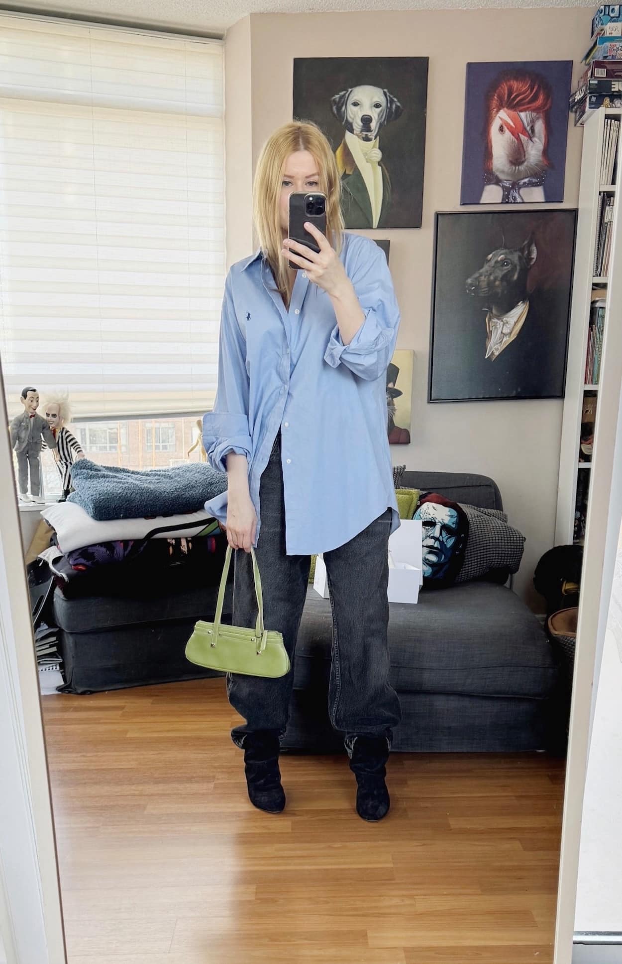 Sara of livelovesara is standing in front of a mirror taking a photo of her outfit. She is wearing a blue button up, black vintage Levis, black boots, and a green baguette bag.