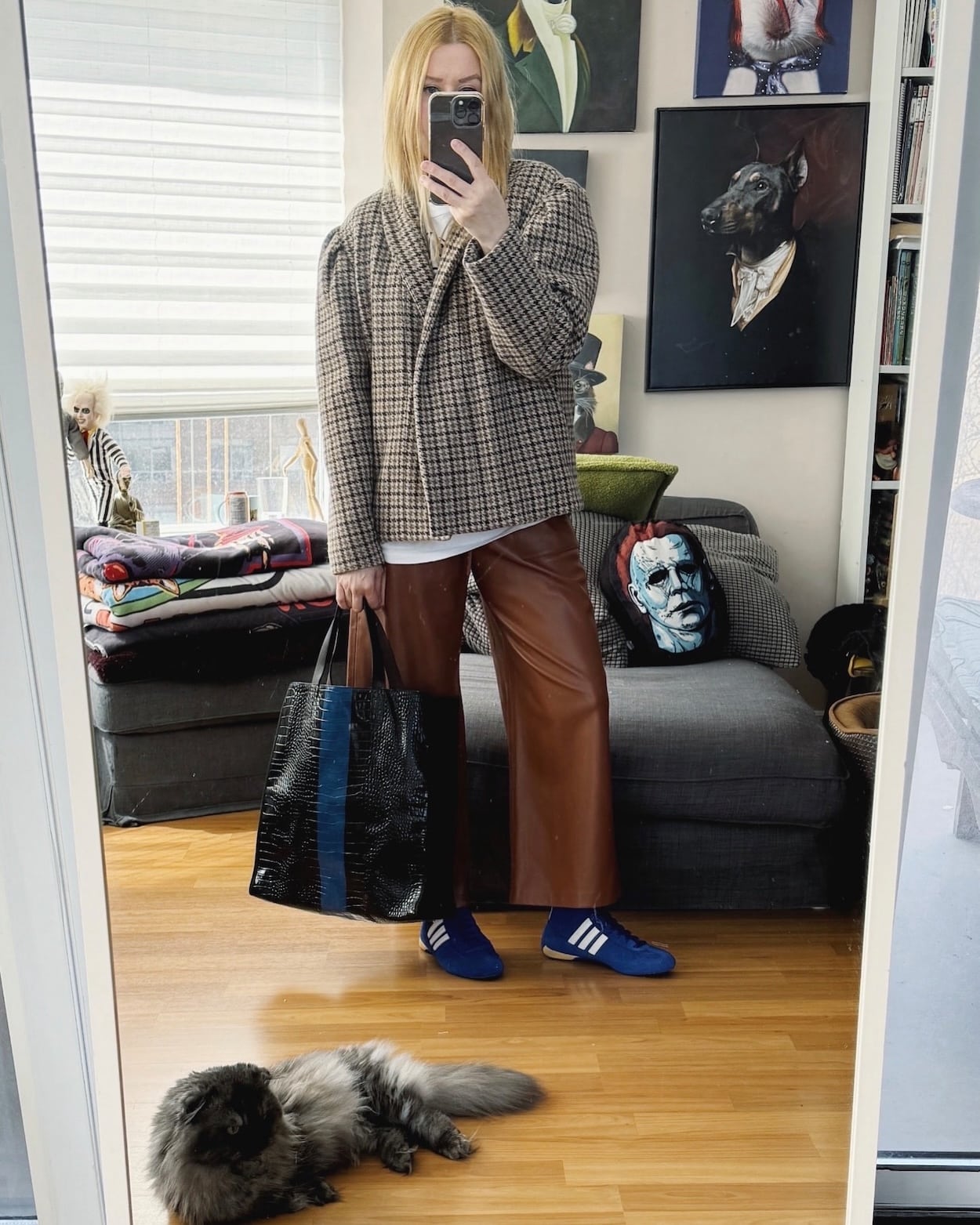 Sara of livelovesara is standing in front of a mirror taking a photo of her outfit. She is wearing a vintage tee with cognac leather trousers, a isabel amrant checkered jacket, blue Adidas wrestling shoes, and a Dries Van Noten tote.