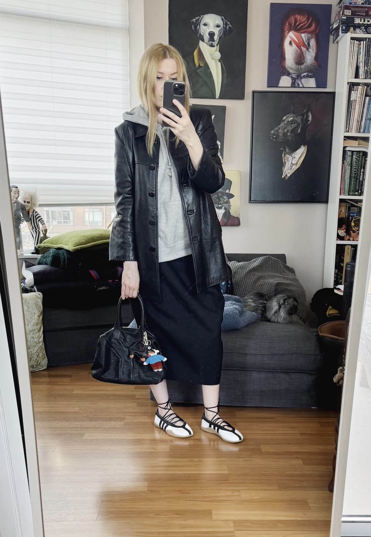 Sara of livelovesara is standing in front of a mirror taking a photo of her outfit. She is wearing a sleeveless hoodie under a black leather blazer, a black midi skirt, Adidas ballet flats, and a YSL easy bag.