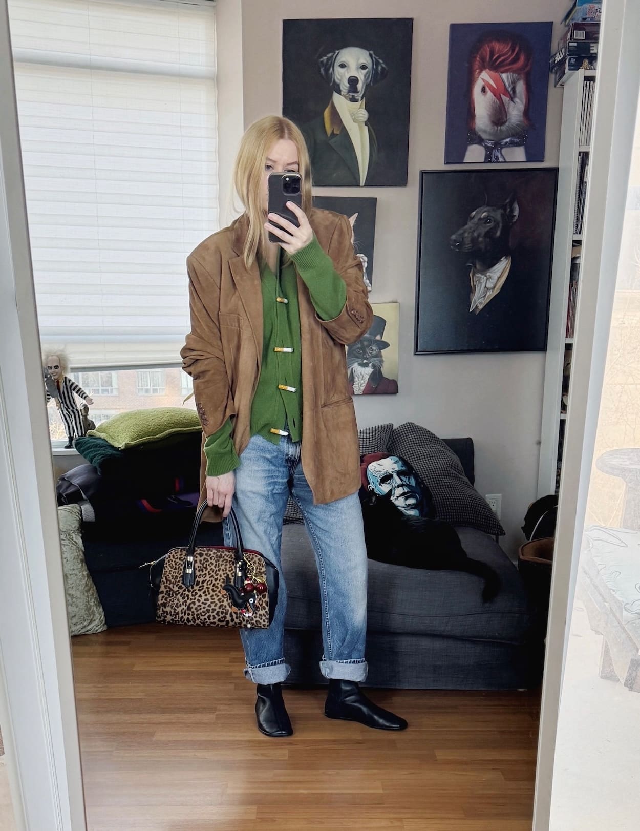 Sara of livelovesara is standing in front of a mirror taking a photo of her outfit. She is wearing a Hades Wool Cigarette Button cardigan under a suede blazer, vintage jeans, black flat boots, and a Ferragamo animal print bag.