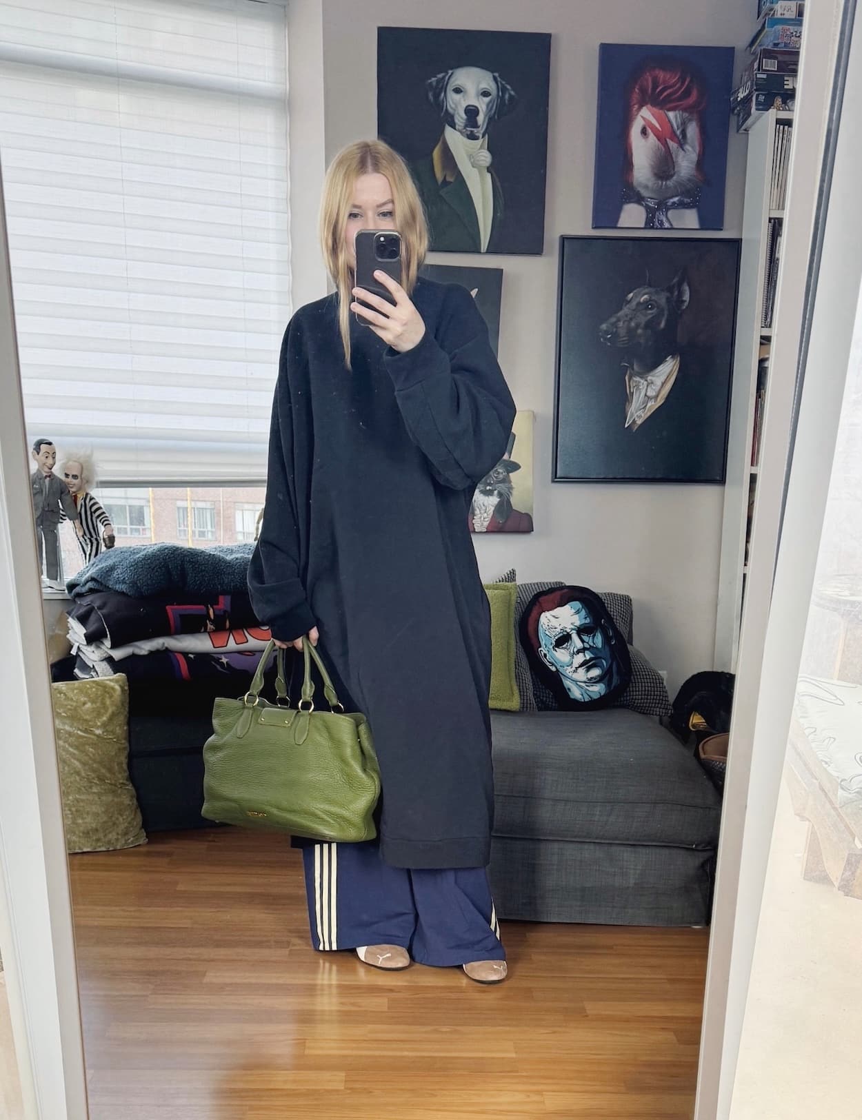 Sara of livelovesara is standing in front of a mirror taking a photo of her outfit. She is wearing an oversized sweatshirt dress over Adidas track pants, brown Puma Speedcats, and is carrying a green tote.