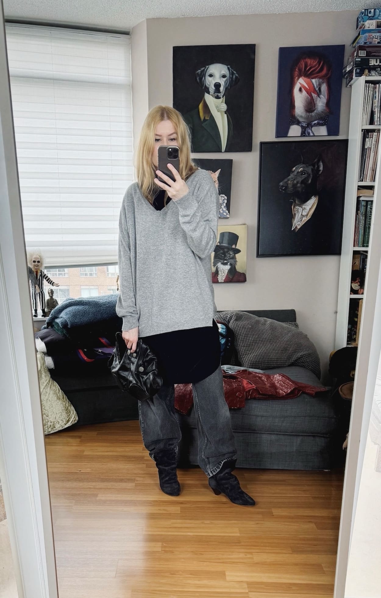 Sara of livelovesara is standing in front of a mirror taking a photo of her outfit. She is wearing a black tunic under a grey sweater, black vintage jeans, Isabel Marant boots, and an Alexander McQueen clutch.