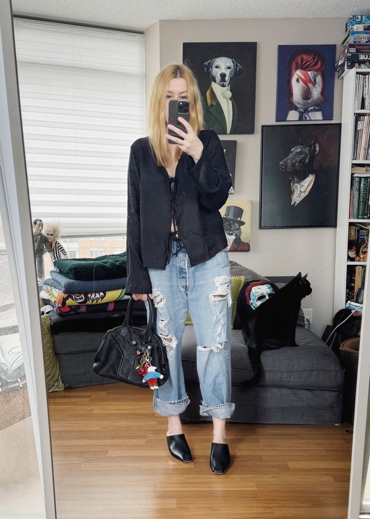 Sara of livelovesara is standing in front of a mirror taking a photo of her outfit. She is wearing a black linen shirt with vintage Levis, black mules, and a vintage bag with bag charms.