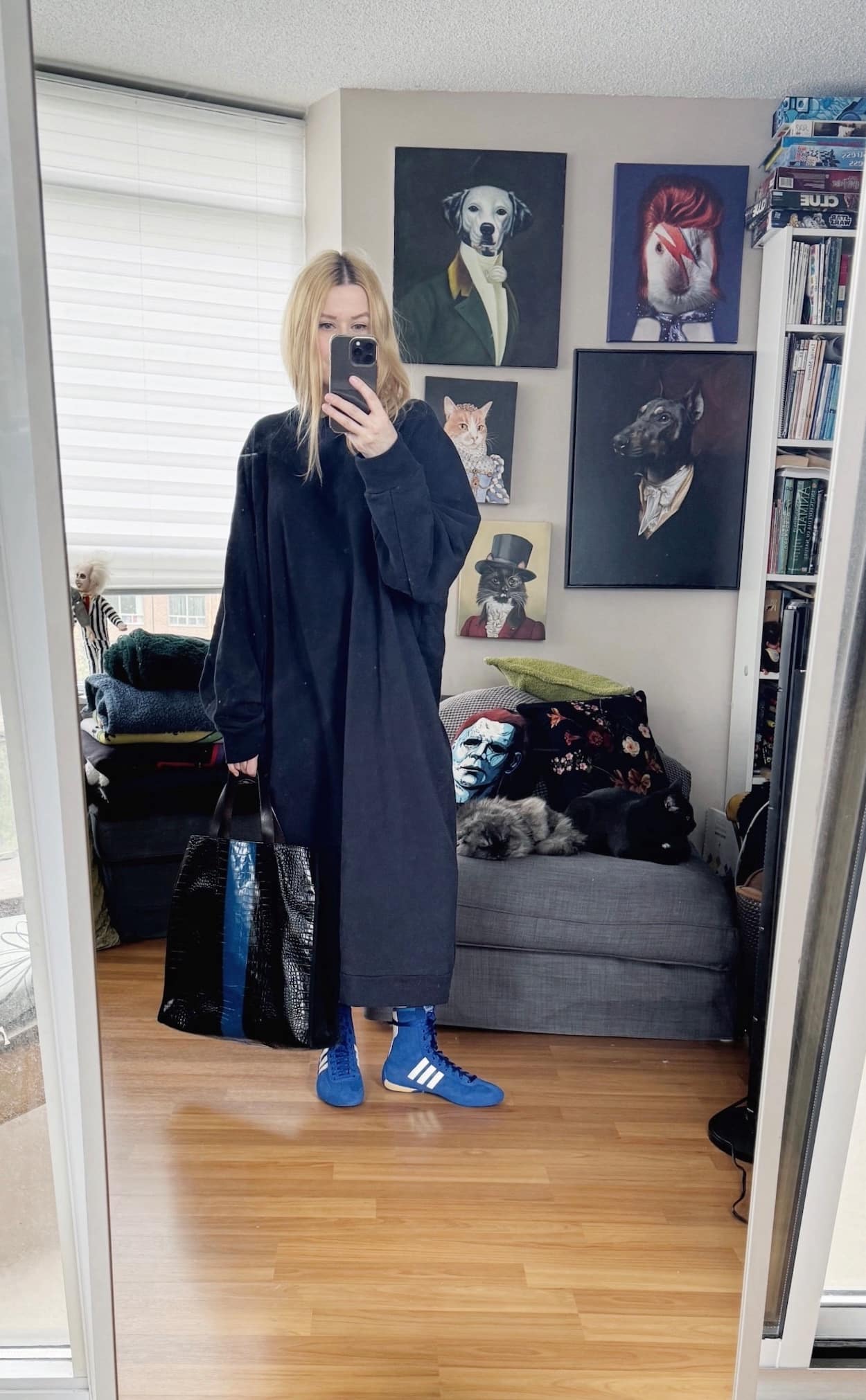 Sara of livelovesara is standing in front of a mirror taking a photo of her outfit. She is wearing a sweatshirt dress, blue Adidas Rasant, and a striped bag/