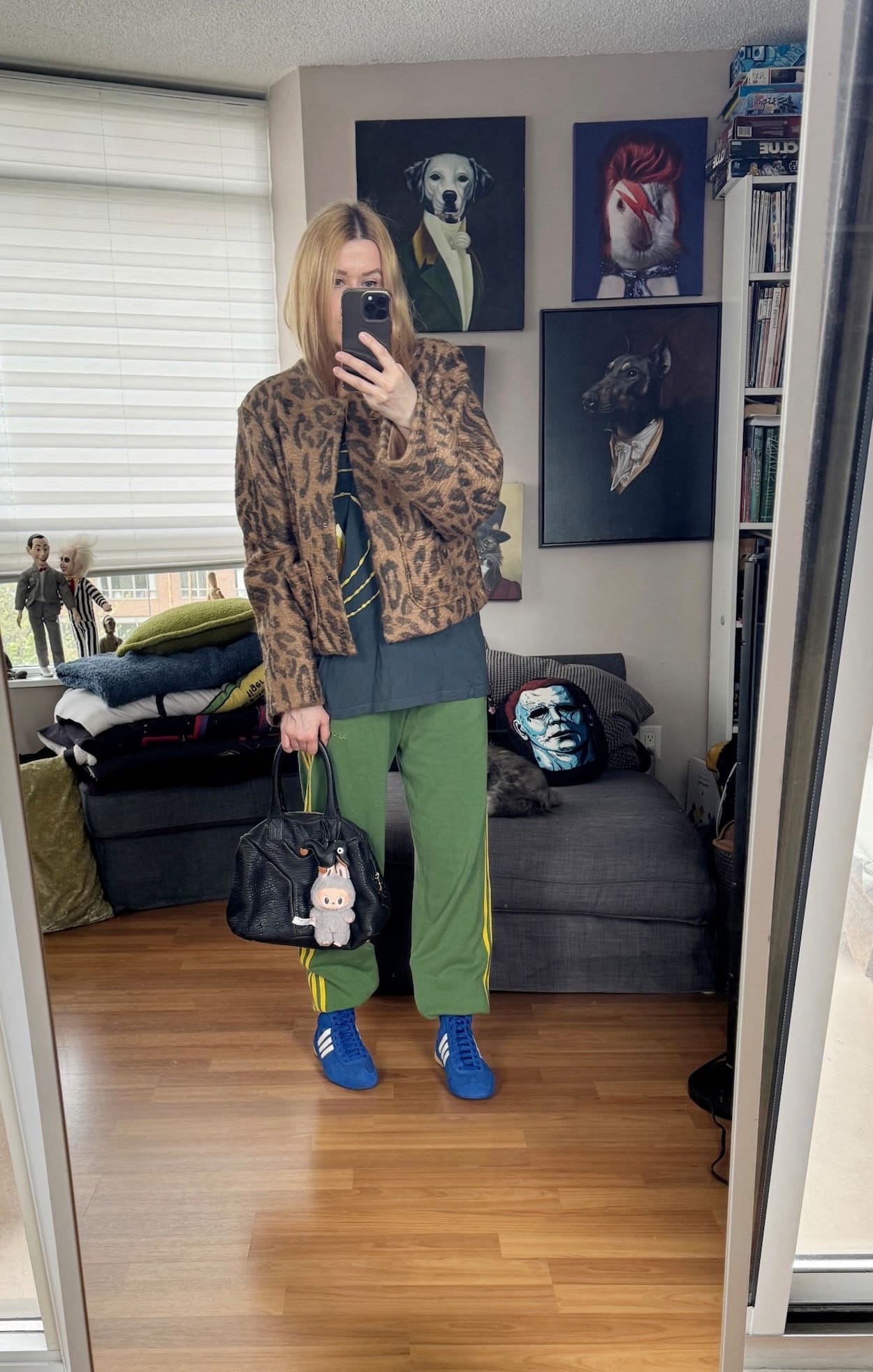 Sara of livelovesara is standing in front of a mirror taking a photo of her outfit. She is wearing a Tori Amos tee with green Adidas track pants, an animal print jacket, blue Adidas sneakers, and a YSL easy bag.