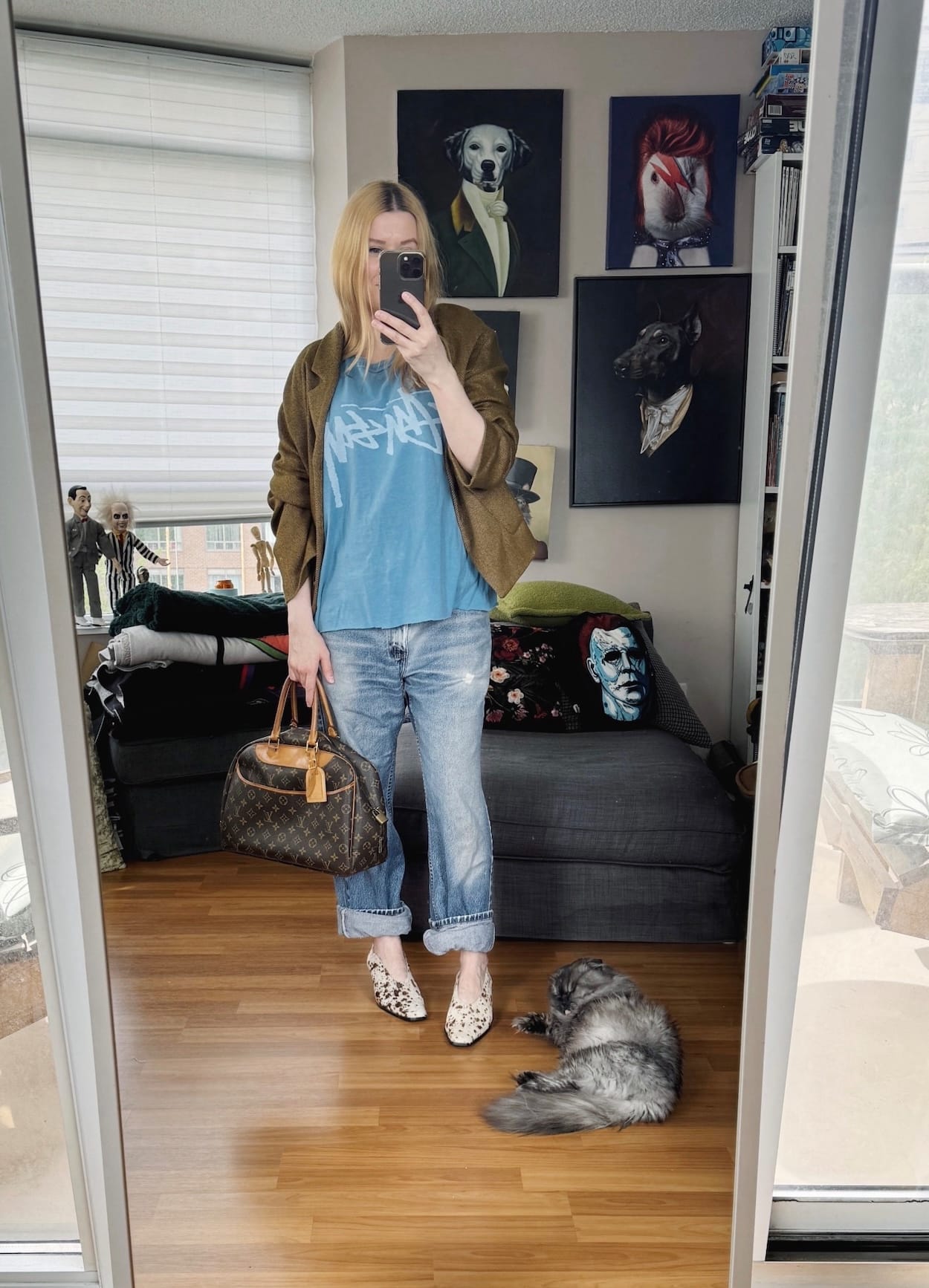 Sara of livelovesara is standing in front of a mirror taking a photo of her outfit. She is wearing a Stussy shirt under a brown coat, vintage levis, animal print heels, and a vintage Louis Vuitton bag.